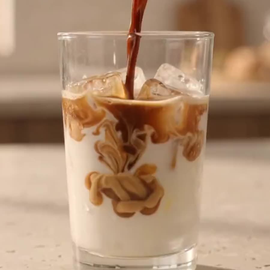 Espresso being poured into a tall glass of iced milk